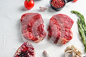 Raw rumpsteak, farm beef meat with seasonings, rosemary, garlic, garnet. White textured background. Side view