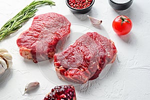 Raw rumpsteak, farm beef meat with seasonings, rosemary, garlic, garnet. White textured background. Side view