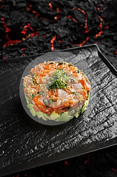 Raw salmon, avocado onion salad served in culinary ring on black plate. Black  background. Tartar