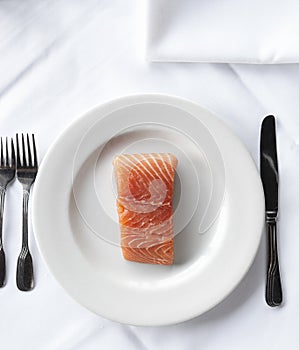 Raw salmon filet on a white plate and linen