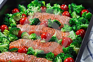 Raw salmon fillet with broccoli and tomato on frying tray, ready to bake, horizontal, closeup