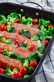 Raw salmon fillet with broccoli and tomato on frying tray, ready to bake, vertical
