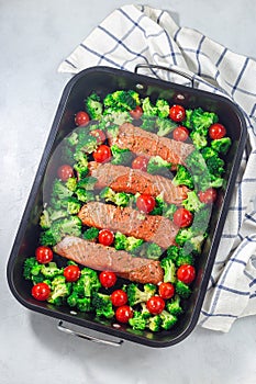 Raw salmon fillet with broccoli and tomato on frying tray, ready to bake, vertical, top view