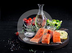 Raw salmon fillet and ingredients for cooking on a dark background