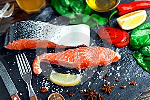 Raw salmon fillet and ingredients for cooking on a dark background in a rustic style.