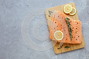 Raw salmon fillet with lemon, rosemary and pepper on cutting board. Fresh organic wild Atlantic fish on grey stone
