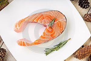 Raw salmon fillet on white square plate with rosemary