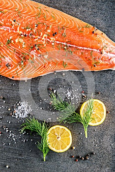 Raw salmon fish steak with ingredients like lemon, pepper, sea salt and dill on black board, modern gastronomy in restaurant