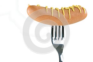 Raw sausage decorated with mustard pierced on a fork, isolated o