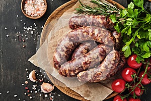 Raw sausages or bratwurst and ingredients for cooking on dark stone background. Top view with copy space