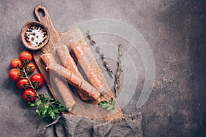 Raw sausages with cherry tomatoes and spices on a cutting board, rustic background. Top view, flat lay,copy space