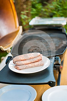 Raw sausages on a plate next to the barbecue