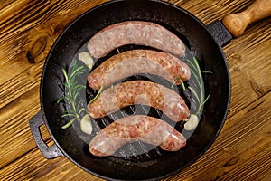 Raw sausages ready for preparation with rosemary, garlic and spices in cast iron grill frying pan on wooden table. Top view