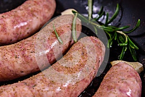 Raw sausages with rosemary twigs and garlic in a cast iron grill pan