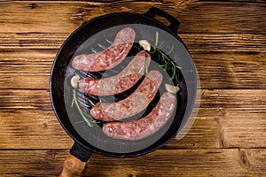 Raw sausages with rosemary twigs and garlic in a cast iron grill pan. Top view