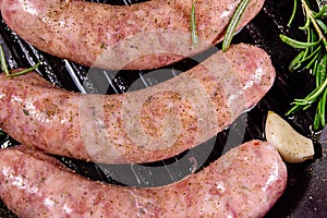 Raw sausages with rosemary twigs and garlic in a cast iron grill pan. Top view