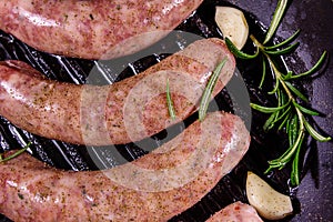 Raw sausages with rosemary twigs and garlic in a cast iron grill pan. Top view