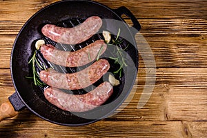 Raw sausages with rosemary twigs and garlic in a cast iron grill pan. Top view