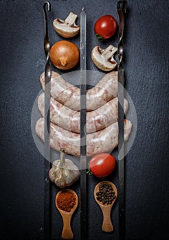 Raw sausages with skewers, different vegetables, spices and ingredients on a black background