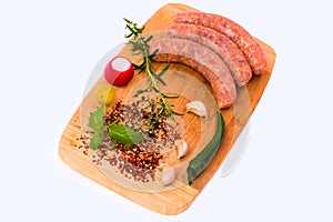 Raw sausages with vegetables on wooden cutting board