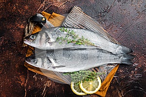 Raw Sea Bass, Branzino fish with thyme and lemon. Dark background. Top view