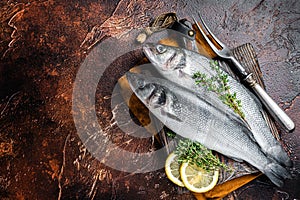 Raw Sea Bass, Branzino fish with thyme and lemon. Dark background. Top view. Copy space