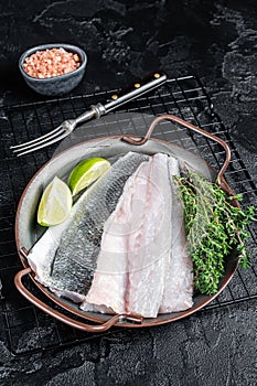 Raw Sea Bass fillet, Labrax fish with herbs and lime. Black background. Top view