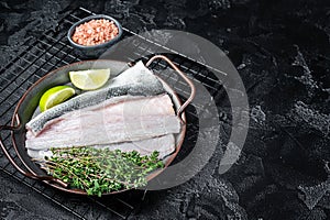 Raw Sea Bass fillet, Labrax fish with herbs and lime. Black background. Top view. Copy space