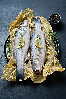 Raw sea bass with rosemary, thyme and lemon. Black background, top view.