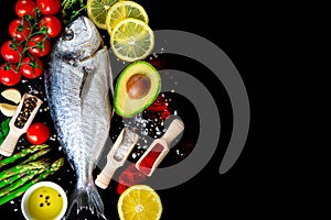Raw sea bream fish on black background with fresh vegetables and spices
