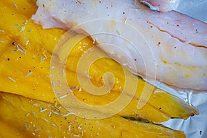 Raw seasoned fish fillets on baking tray closeup