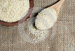 Raw sesame seeds in wooden shovel and bowl on burlap sack