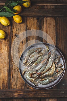 Raw shrimps prawns on gray plate with lemons and cilantro. Top view , wooden background