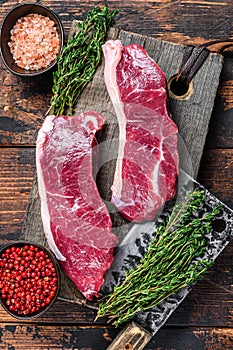 Raw sirloin beef meat steak on a wooden cutting board with herbs. Dark wooden background. Top view