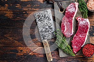 Raw sirloin beef meat steak on a wooden cutting board with herbs. Dark wooden background. Top view. Copy space