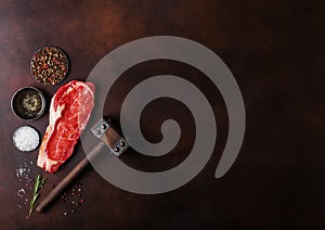 Raw sirloin beef steak with meat hammer on rusty background. Salt and pepper with fresh rosemary and bowl of oil.Space for text
