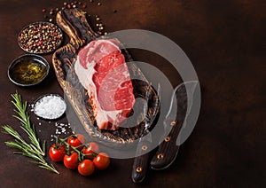 Raw sirloin beef steak on old vintage chopping board with knife and fork on rusty background. Salt and pepper with fresh rosemary
