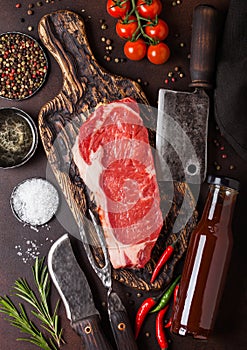 Raw sirloin beef steak on vintage chopping board with knife and fork on rusty background. Salt and pepper with fresh rosemary and