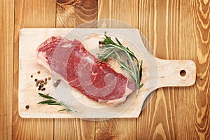 Raw sirloin steak with rosemary and spices on cutting board