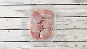 Raw skinless boneless chicken thighs in plastic container close-up on white wooden board, copy space