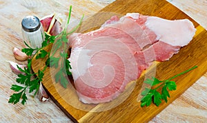 Raw slice of Iberian pork secret on wooden cutting board with seasonings