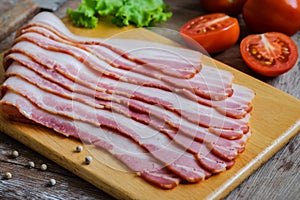 Raw sliced bacon on wooden board