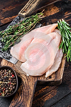 Raw sliced cut chicken breast fillet cutlets on a wooden cutting board with cleaver. Dark wooden background. Top view