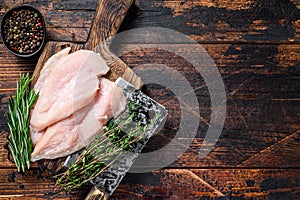 Raw sliced cut chicken breast fillet cutlets on a wooden cutting board with cleaver. Dark wooden background. Top view