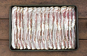 Raw sliced peppercorn bacon in baking sheet