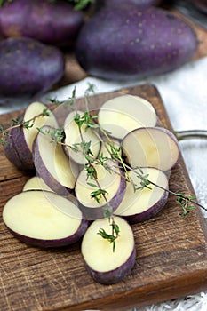 Raw sliced potato on wooden board, thyme seasoning.