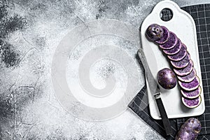 Raw sliced purple potatoes on a white chopping Board. Gray background. Top view. Space for text