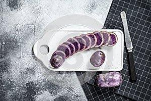 Raw sliced purple potatoes on a white chopping Board. Gray background. Top view. Space for text