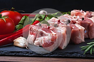 Raw slices of pork on a black slate board, tomatoes, red pepper and powder. Pork belly with vegetables