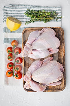 Raw small young chicken with herbs and ingredients, on white background, top view